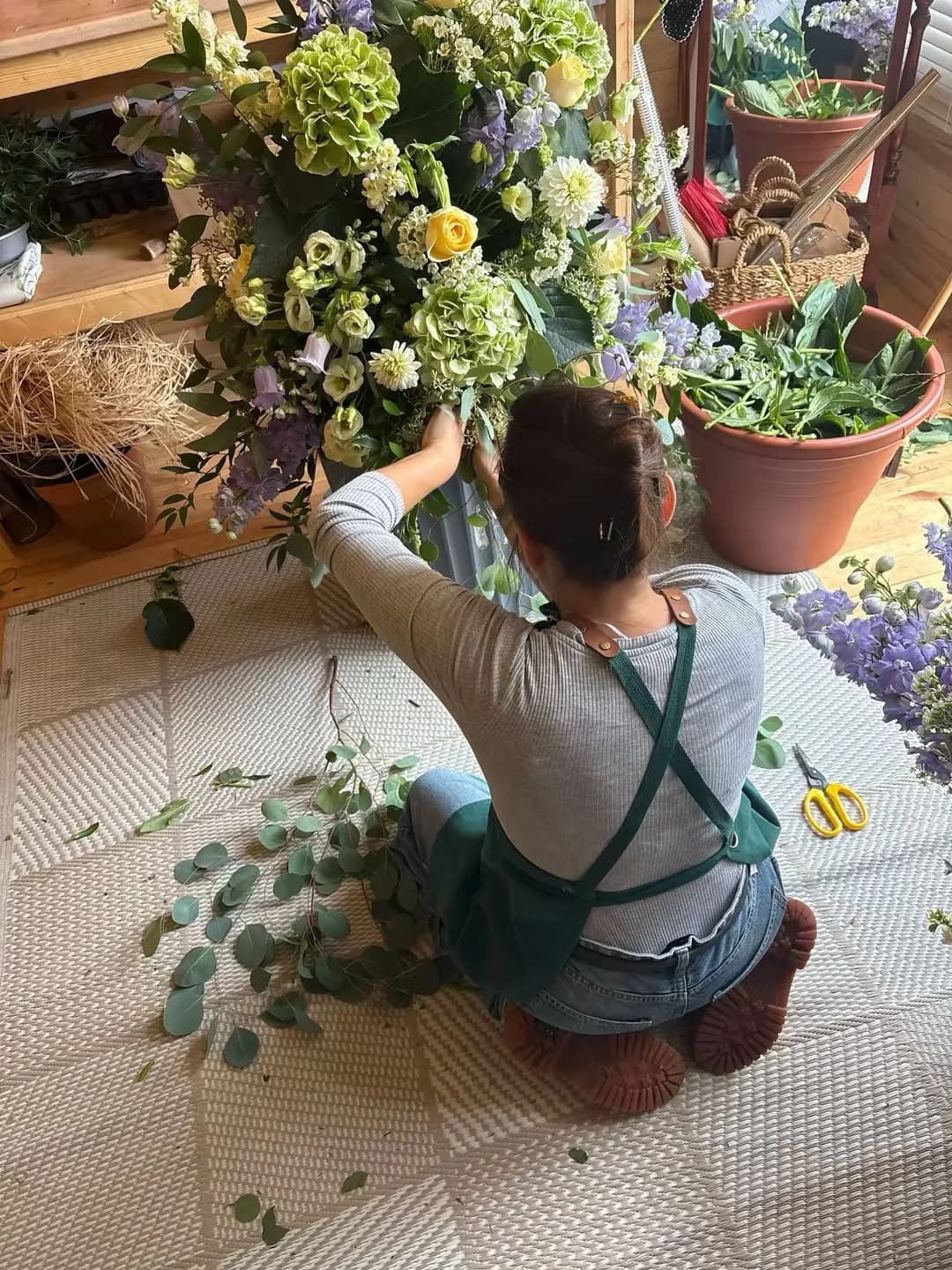 A florist assembling a large pastel wedding arrangement in the studio