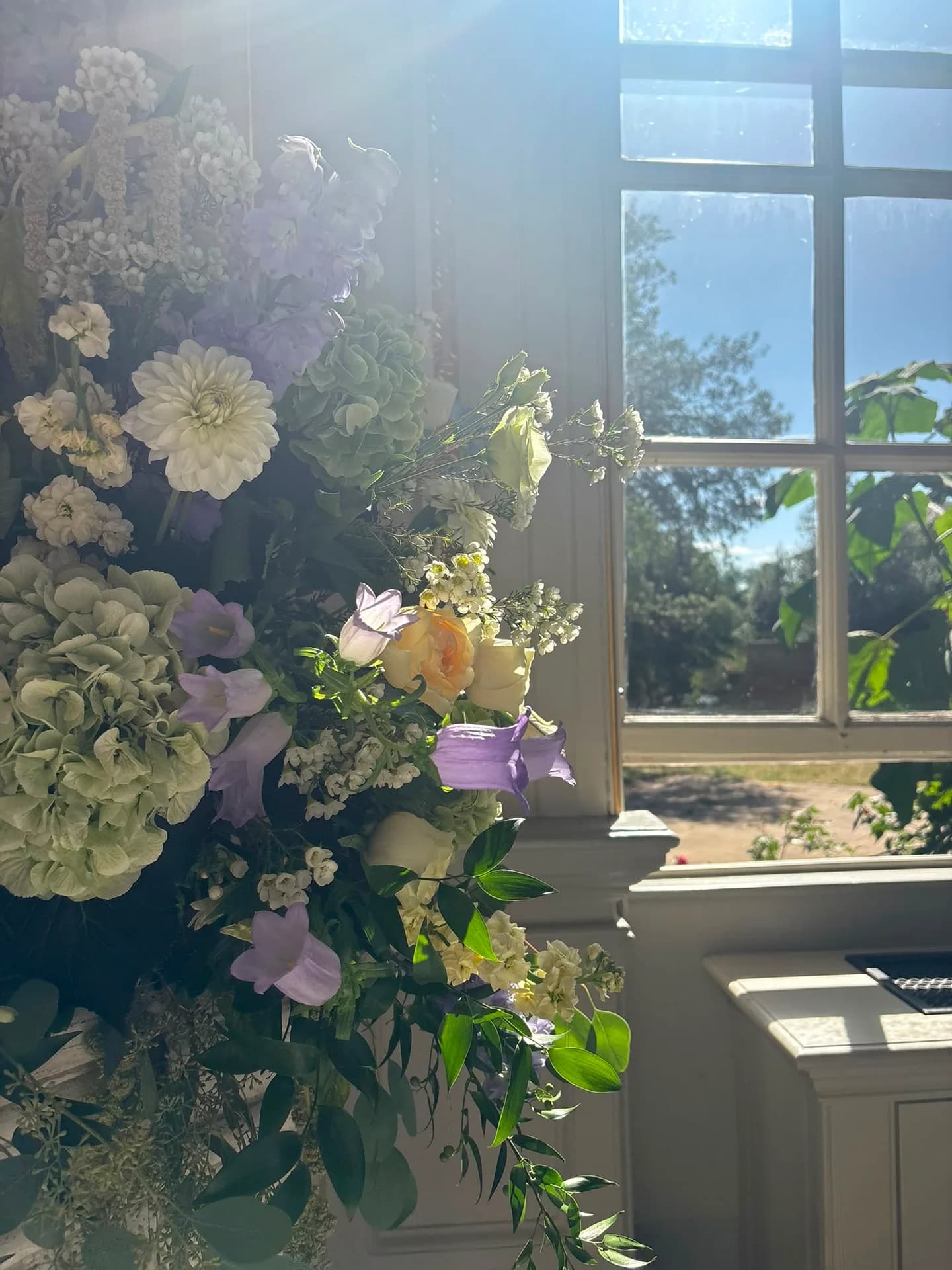 Sunlight falling across a pastel wedding flower arrangement beside a tall window