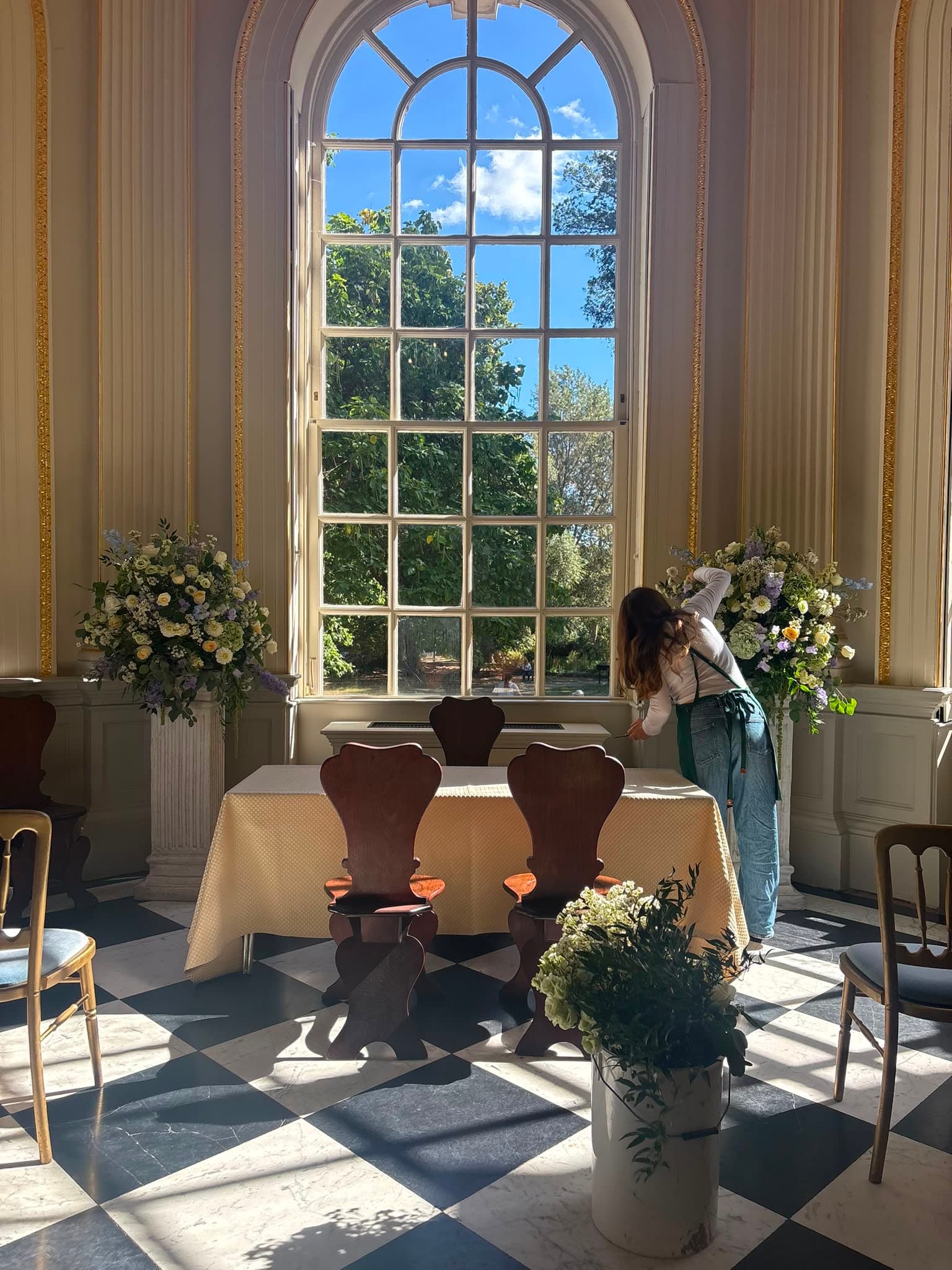 A florist placing the finishing touches on wedding ceremony flowers beside a tall window