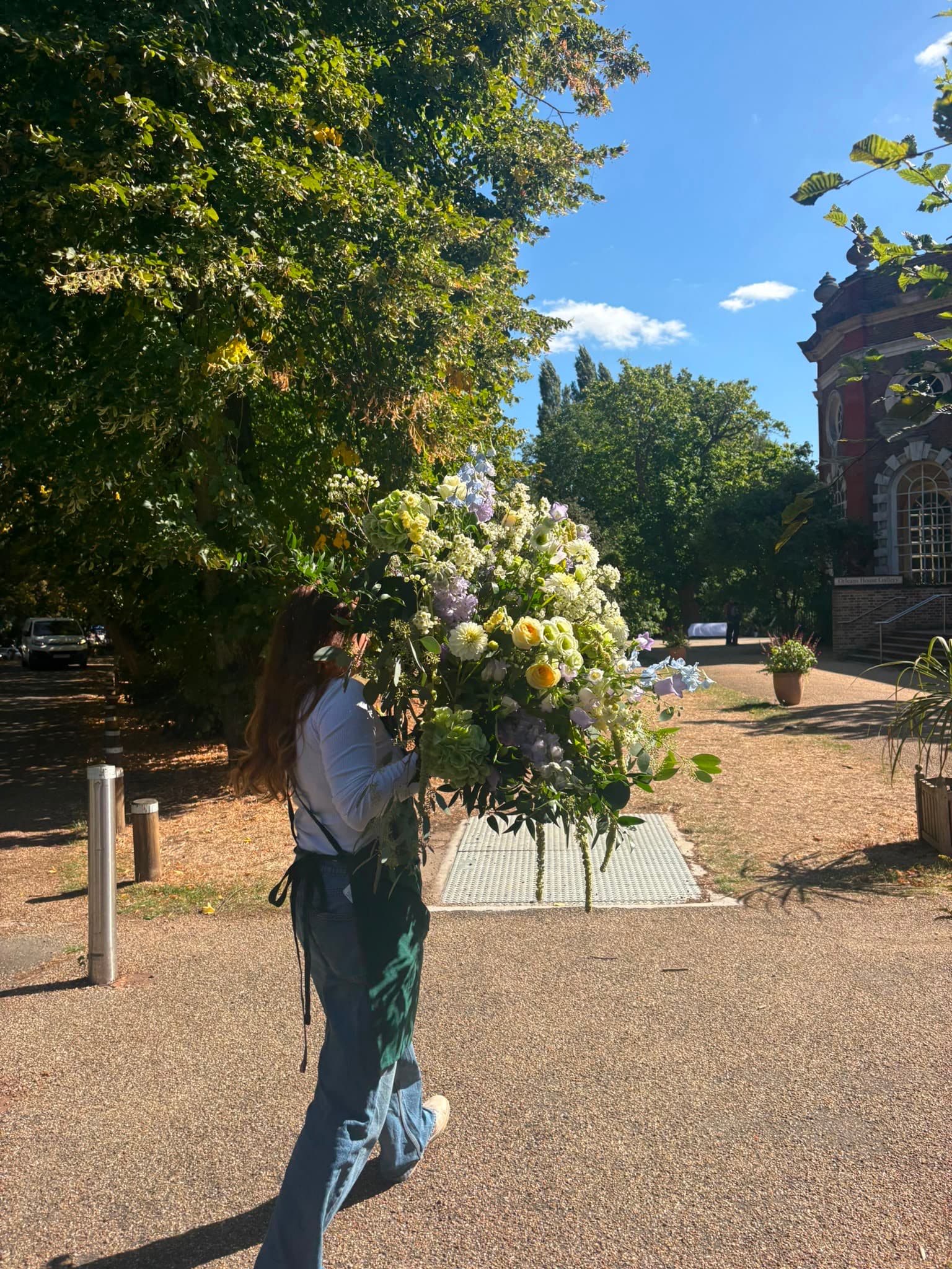 A florist carrying green, white and pale yellow wedding flowers outside a brick venue